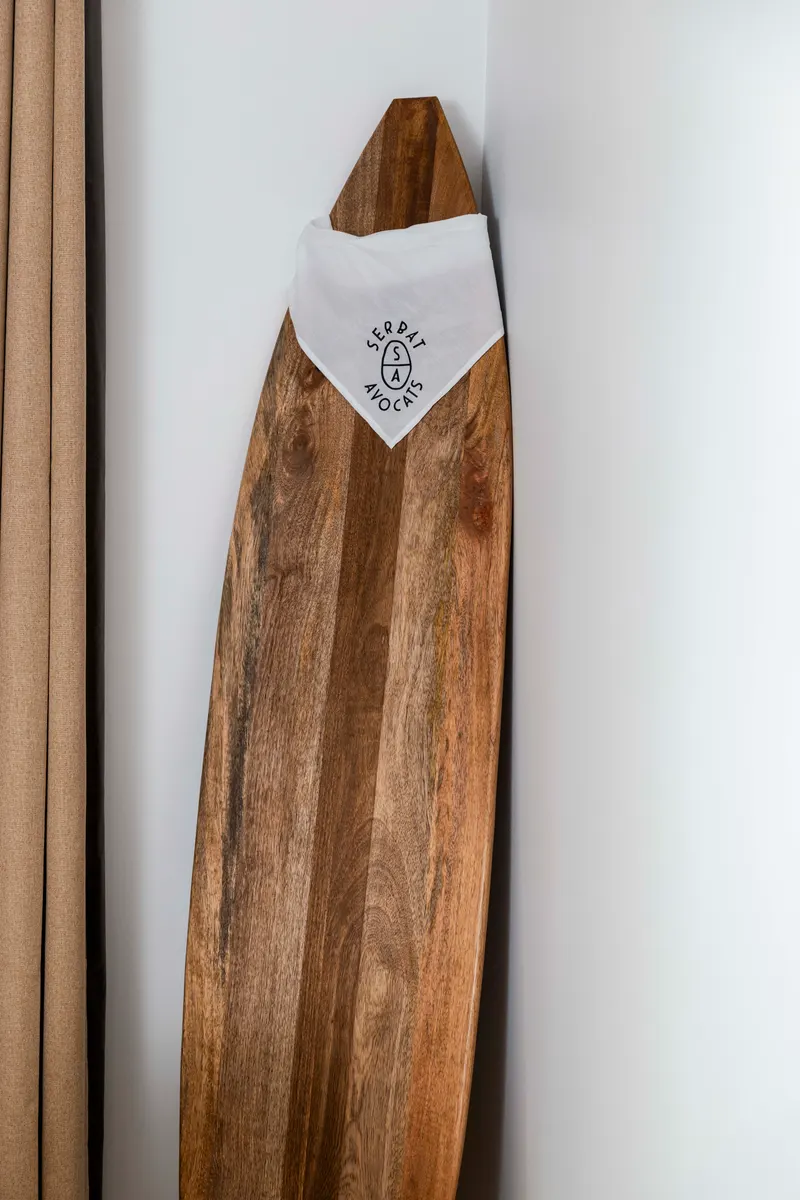 Planche de surf en bois portant le bandana Serbat Avocats, clin d’œil aux Landes